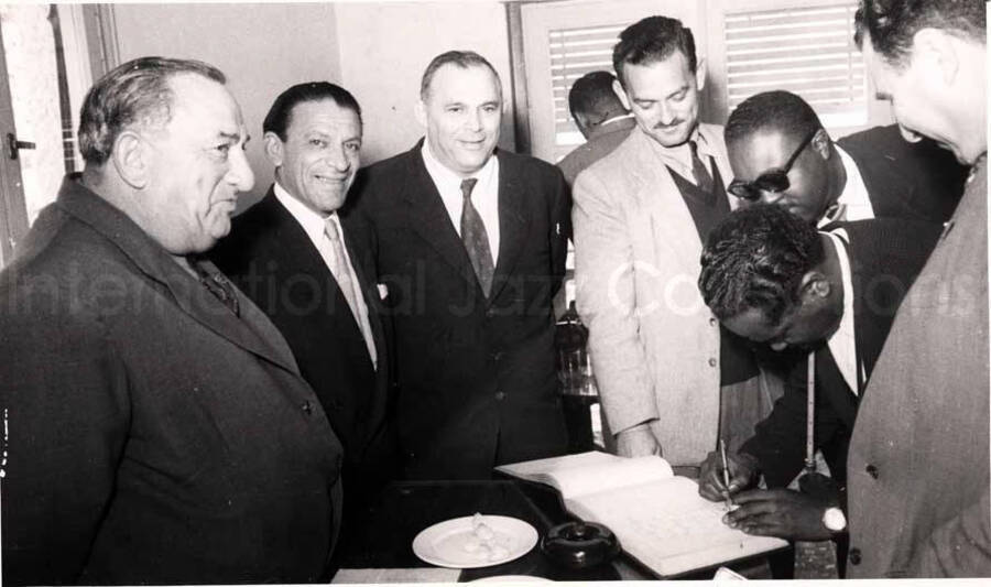 5 x 8 inch photograph. Gladys and Lionel Hampton with band in Israel. A member of the Lionel Hampton's band signing a book with unidentified men