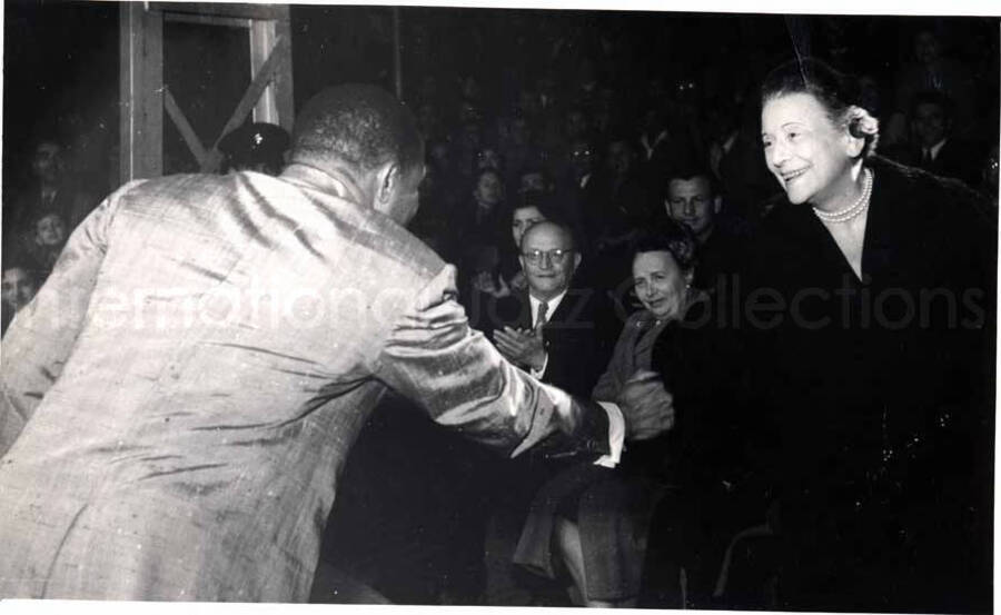 5 x 8 inch photograph. Lionel Hampton performing with band in Israel. Lionel Hampton shakes hands with unidentified woman in the audience
