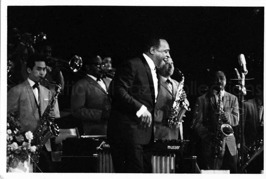 3 x 5 inch photograph. Lionel Hampton on stage with band playing in the background [in Japan?]