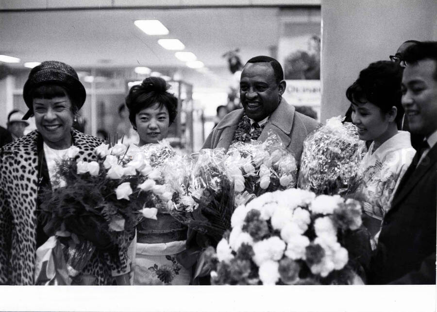 4 1/2 x 6 1/2 inch photograph. Gladys and Lionel Hampton are welcomed with flowers at an airport terminal [in Japan]