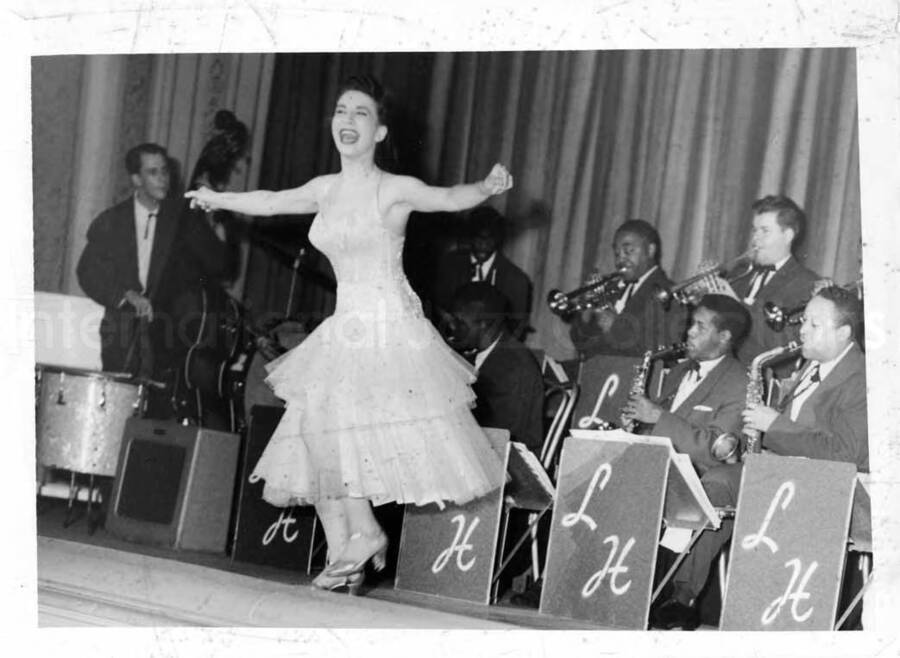 5 x 7 inch photograph. Unidentified woman dancing on stage with Lionel Hampton's orchestra. Handwritten on the back of the photograph: Dear Sugar, very rough proofs more to follow, Bernie