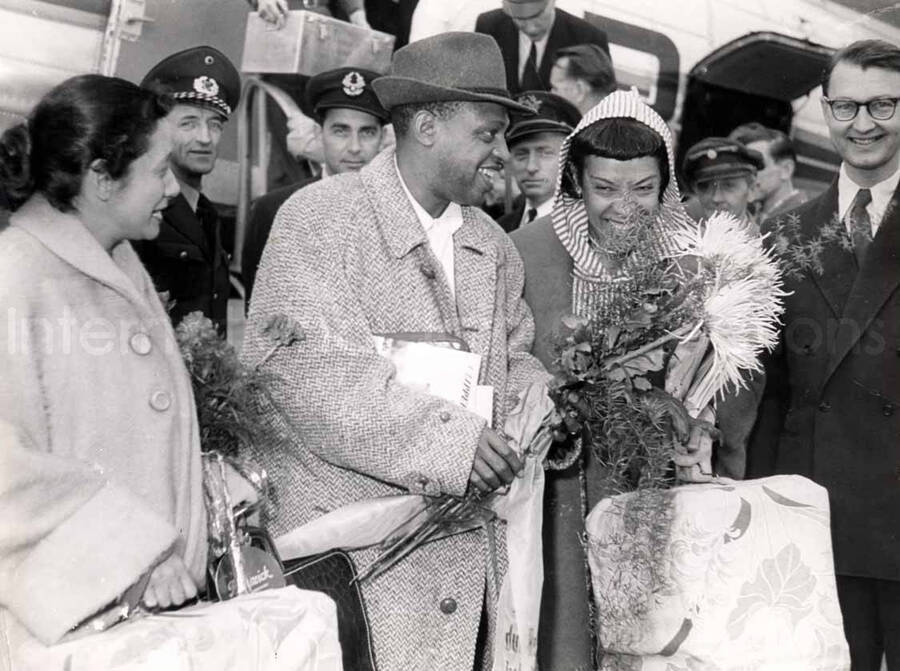 5 3/4 x 7 3/4 inch photograph. Gladys and Lionel Hampton with unidentified persons, walking outside an airport [in Germany?]