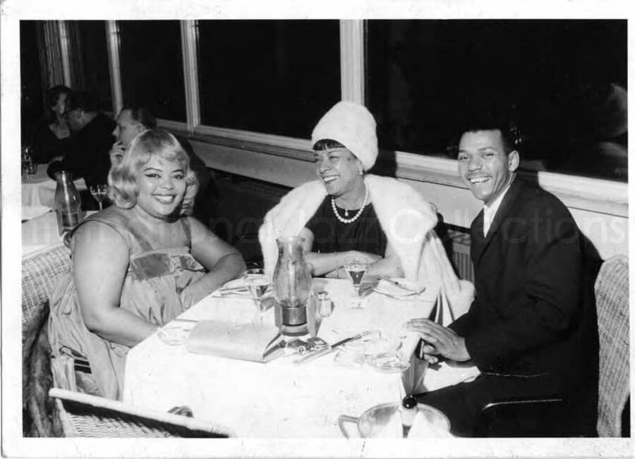 4 x 6 inch photograph in the format of postcard. Gladys Hampton and Leo Moore with unidentified woman at the restaurant of the Hilton Hotel in Berlin, Germany