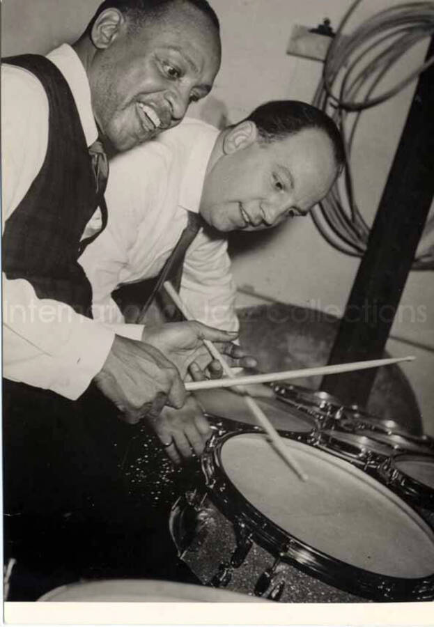 5 1/2 x 4 inch photograph. Lionel Hampton playing the drums as an unidentified man looks on. [in Germany?]