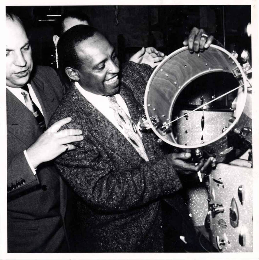7 x 7 inch photograph. Lionel Hampton looking at various types of drums [in Germany?]
