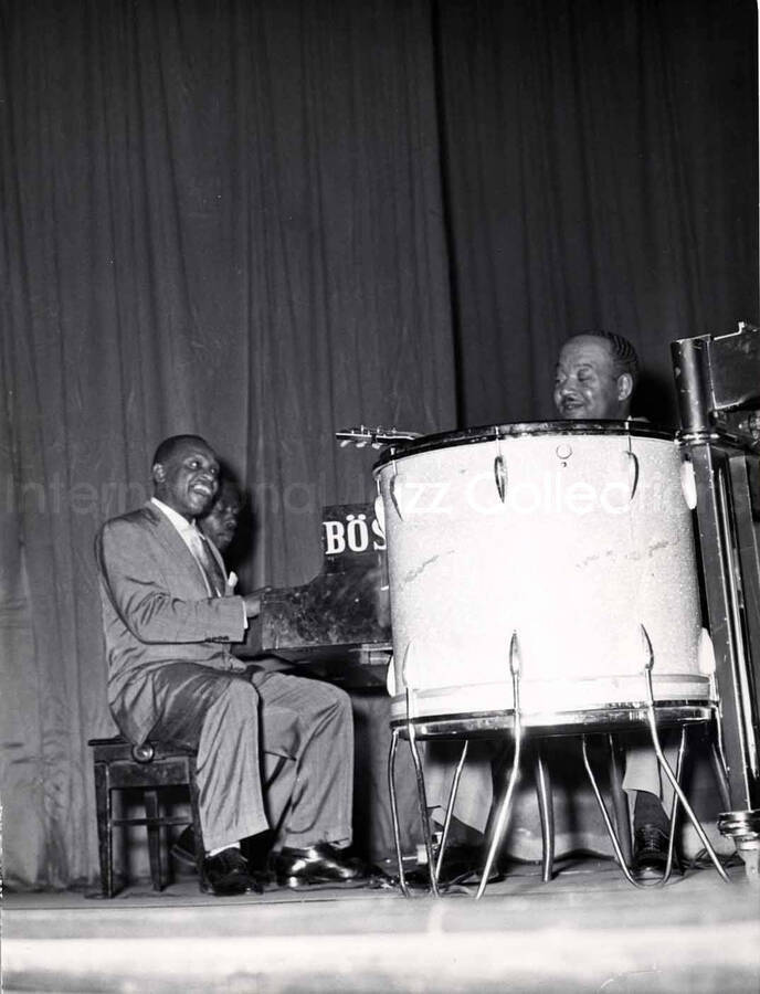 9 1/2 x 7 inch photograph. Lionel Hampton on piano with unidentified pianist. Guitarist Billy Mackel behind a  set of Trixon drums. [Milan, Italy?]