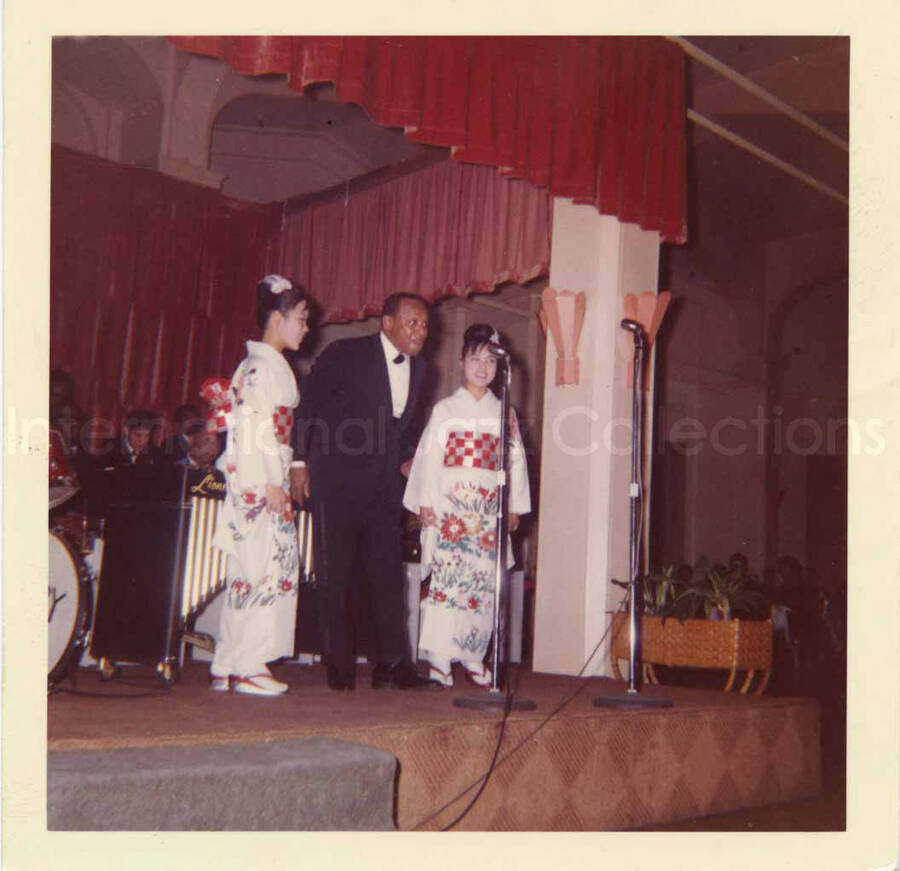 3 1/2 x 3 1/2 inch photograph. Lionel Hampton's Band [in Japan]. Lionel Hampton with two unidentified women dressed in Japanese costume