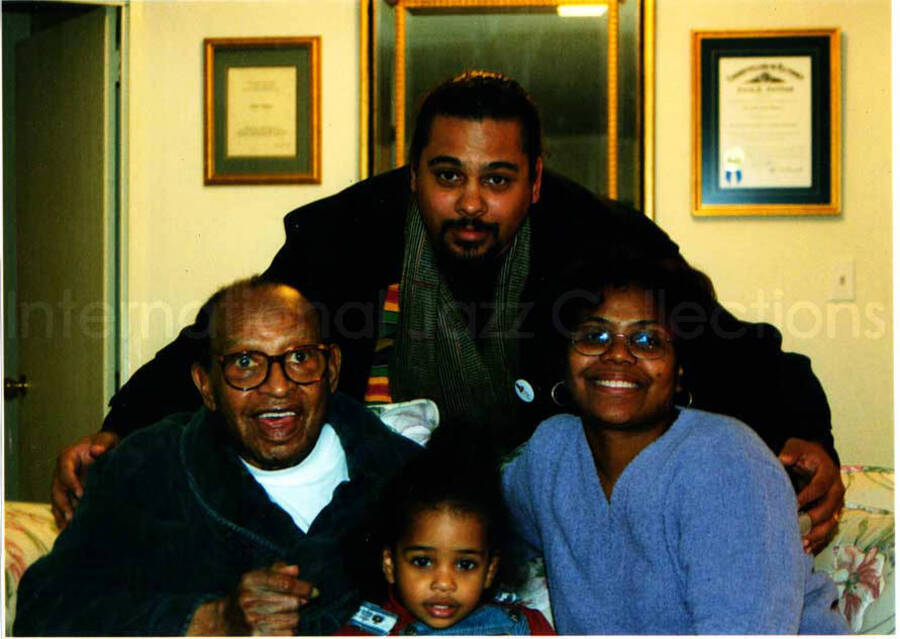 5 x 7 inch photograph. Lionel Hampton with a family in his apartment. Accompanying this photograph is a card of D. Kenneth Jenkins, freelance writer and radio program producer. Handwritten on the back of the card is a dedication to Lionel Hampton from Vashti Jenkins (Dinah Washington's Great Granddaugter) and family. This picture was in a connoisseur frame
