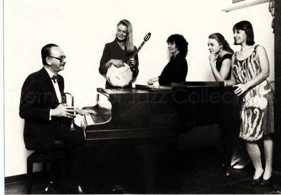 4 x 6 inch photograph. Unidentified group around a piano. Handwritten on the back of the photograph: For a real musical and swinging year 1983 from Yannick and Mazgo's Hot Five!