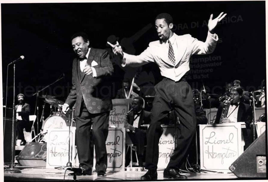 7 x 9 1/2 inch photograph. Lionel Hampton with Chester Whitmore [in Italy]. The background of the stage reads: E ora di America; United Sounds of America