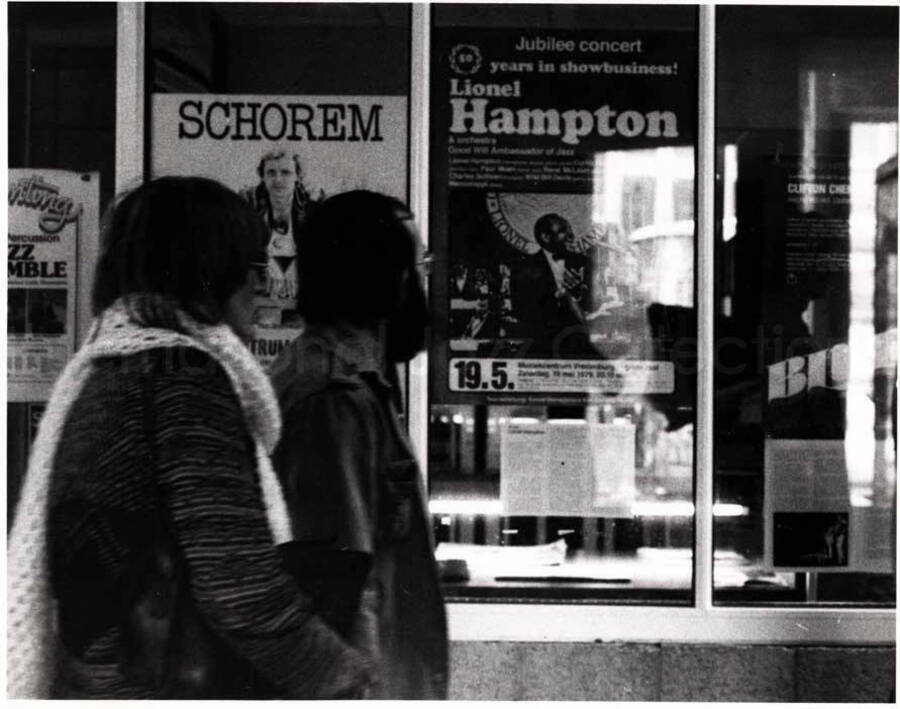4 x 5 1/2 inch photograph. Pedestrians passing by a poster announcing Lionel Hampton jubilee concert. It reads: 50 years in show business; Lionel Hampton and Orchestra; Good Will Ambassador of Jazz [in German?]