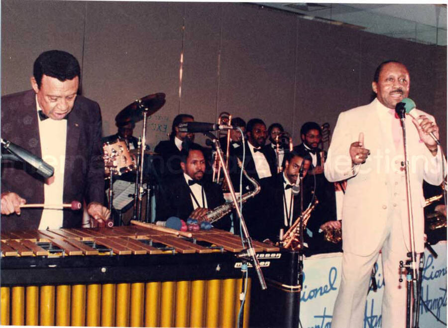 8 x 11 inch photograph. Lionel Hampton on vibraphone with band and unidentified man at the Charles Hotel, Boston. From a scrapbook