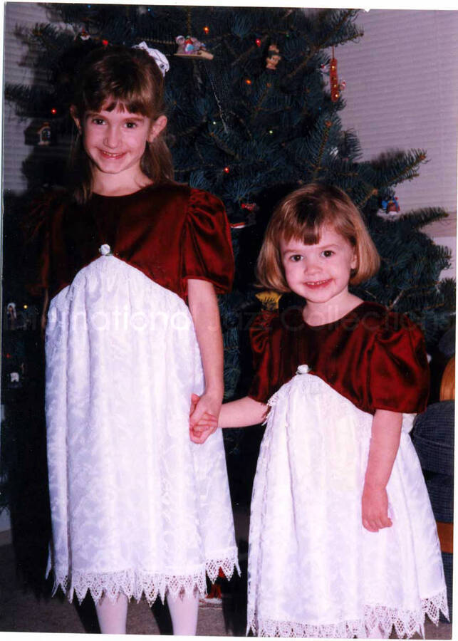 5 x 3 1/2 inch photograph. Two girls posing in front of a Christmas tree