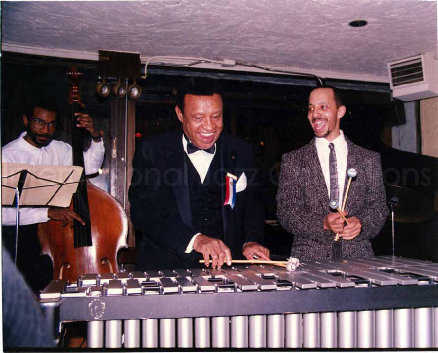8 x 10 inch photograph. Lionel Hampton on vibraphone with unidentified musicians. Lionel Hampton is wearing a name tag with a red, white, and blue ribbon