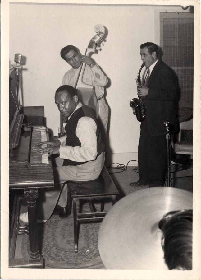 7 x 5 inch photograph. Lionel Hampton playing the piano with unidentified musicians. He has his left foot on cast