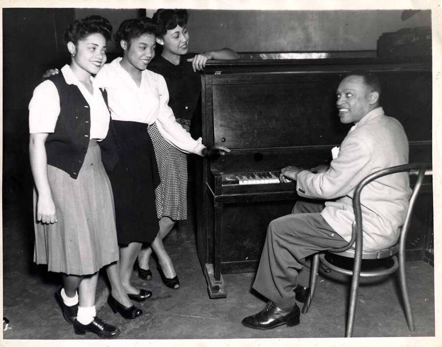 8 x 10 inch photograph. Lionel Hampton playing the piano observed by three unidentified women