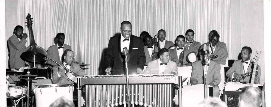 4 x 10 inch photograph. Lionel Hampton playing the vibraphone with band. William (Billy) Mackel plays the guitar.