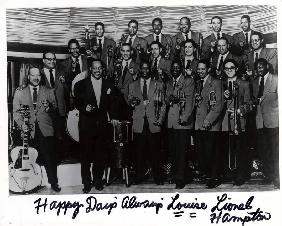 8 x 10 inch photograph. Lionel Hampton's orchestra. Back row from left to right: Jimmy Cleveland, Johnny Board, Benny Bailey, Eddie Mullens, Benny Powell and Al Grey. Middle row from left to right: Milt Buckner (standing between middle and front row, behind Billy Mackel), Roy Johnson (bass), Ben Kenard, Curtis Lowe, Gil Bernal, Bobby Plater, and Jerome Richardson. Front row from left to right: William 'Billy' Mackel (guitar), Lionel Hampton, Al Hayes, Leo Shepherd, Walter Williams, Paul Higaki and Ellis Bartee. Handwritten on the bottom of the photograph: Happy days always Louise; Lionel Hampton