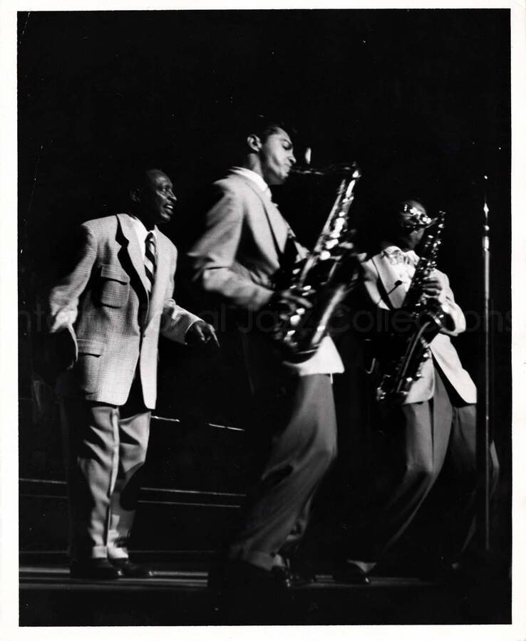 10 x 8 inch photograph. Lionel Hampton with Curtis Lowe on baritone saxophone. Both saxophonists are performing on the baritone saxophone.