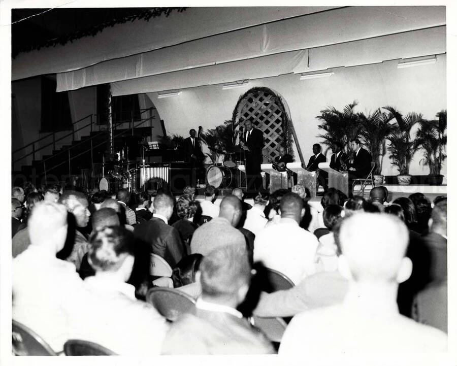 8 x 10 inch photograph. Lionel Hampton playing the drums with band, which includes guitarist Billy Mackel. On the back of the seats of the audience are inscribed the letters: FH