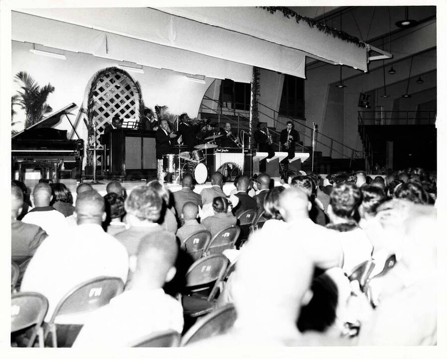 8 x 10 inch photograph. Lionel Hampton on stage with band, which includes guitarist Billy Mackel. On the back of the seats of the audience are inscribed the letters: FH