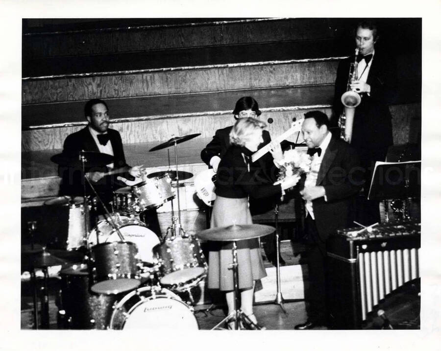 8 x 10 inch photograph. Lionel Hampton receiving flowers from an unidentified woman on stage with band