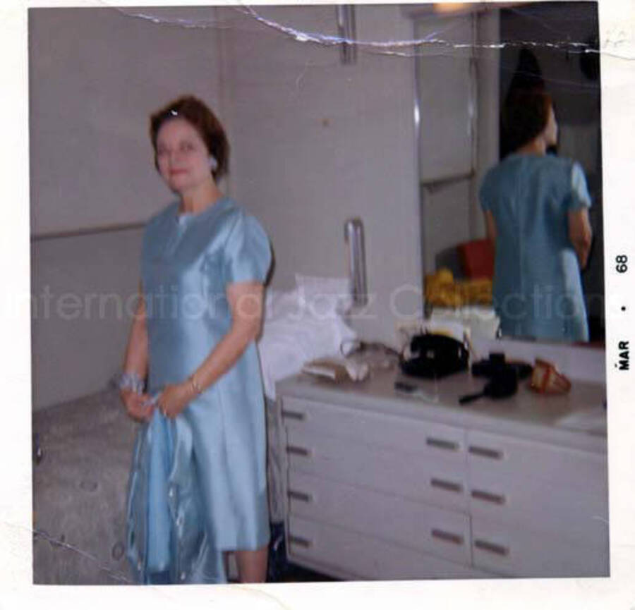 3 1/2 x 3 1/2 inch photograph. Unidentified woman standing in a bedroom. Handwritten on the back of the photograph: Feb. 1968; boat