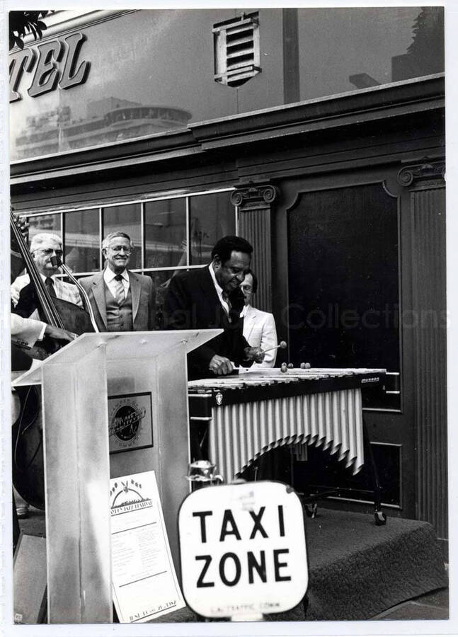 7 x 5 inch photograph. Lionel Hampton on vibraphone on the occasion of his receiving a plaque from the Hollywood Chamber of Commerce. Los Angeles, CA. A poster is visible noting the Playboy Jazz Festival