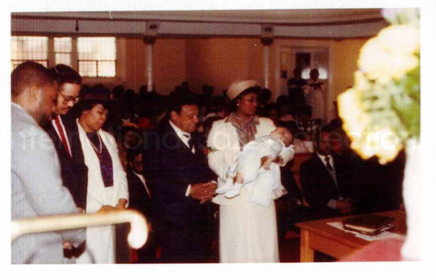 4 x 6 inch photograph. Religious ceremony depicting a woman holding a baby beside Lionel Hampton. Accompanying this photograph is a copy of the certificate of dedication of David Edge, Jr., son of David and Rita Lancaster Edge, having as Godparents Lionel Hampton and Mazie Holland, at the Way of the Cross Church