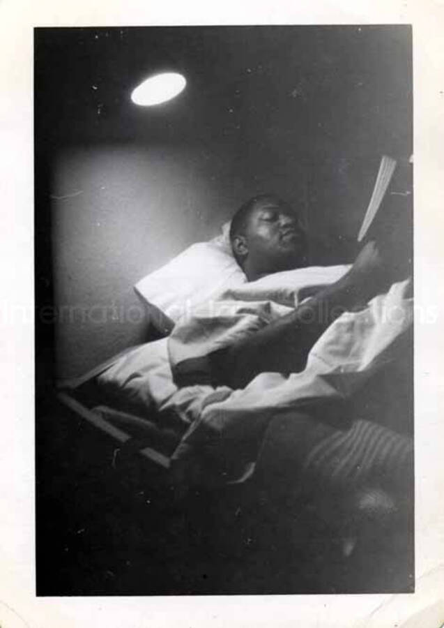 4 1/2 x 3 1/4 inch photograph. Unidentified man on a bunk reading a book