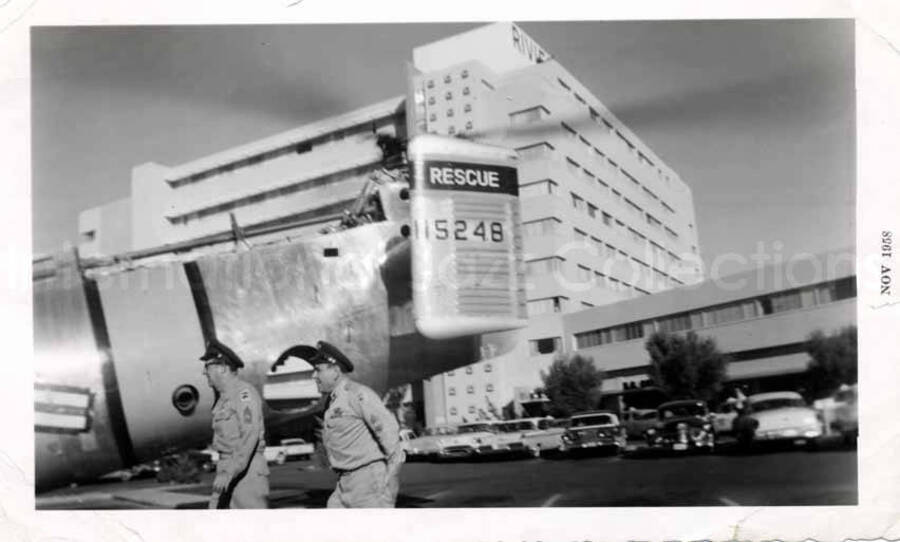 3 1/2 x 5 3/4 inch photograph. Two officers and the back of a rescue aircraft bearing the number 115248, in front of a hotel building named the Rivi[]. Handwritten on the back of the photograph: Good luck; Phil Silvers [?]