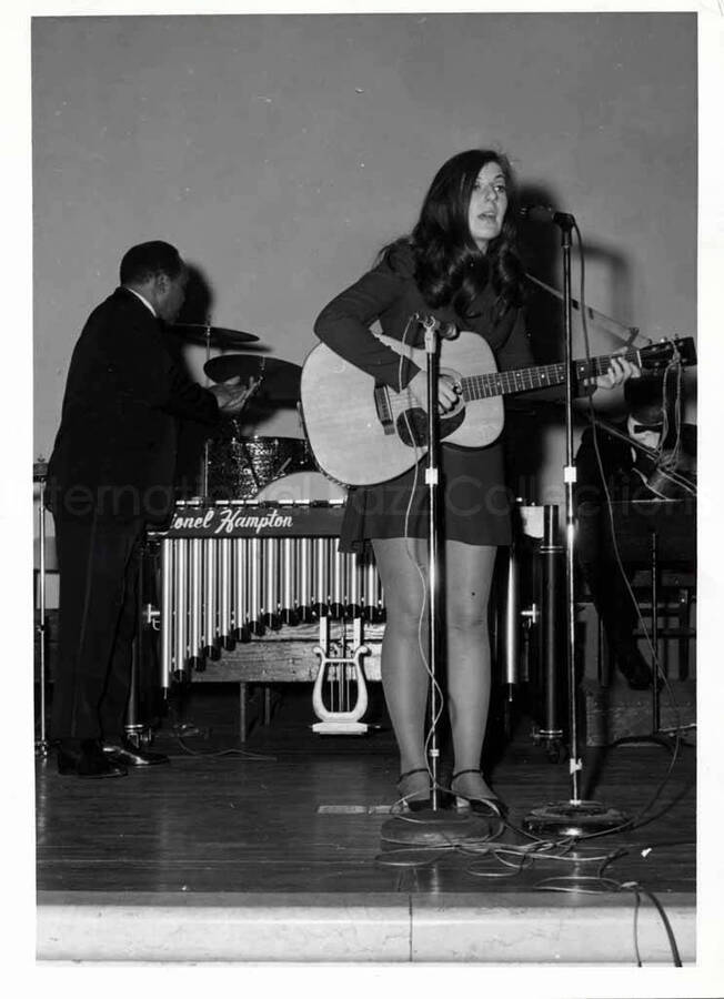7 x 5 inch photograph. Unidentified woman singing with Lionel Hampton in the background