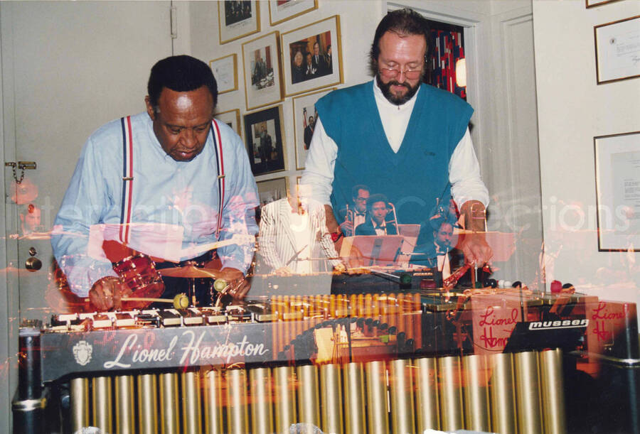 7 x 10 1/2 inch photograph. This is a juxtaposition of images. The main image depicts Lionel Hampton and Jean Claude Forestier playing the vibraphone in Lionel Hampton's apartment. The secondary image shows Lionel Hampton performing with band. This photograph was used also in a calendar (Box 16, Folder 12)