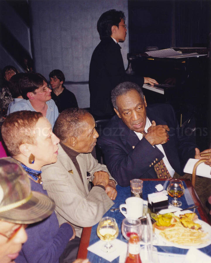 10 x 8 inch photograph. Bill Cosby conversing with unidentified couple. Lionel Hampton's 90th birthday at the Blue Note in New York