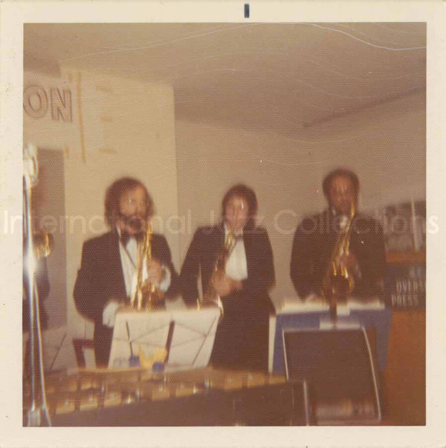 3 1/2 x 3 1/2 inch photograph. Lionel Hampton and band at the Overseas Press Club of America. A banner on the wall reads: Welcome Lionel Hampton, America's Good Will Ambassador of Jazz