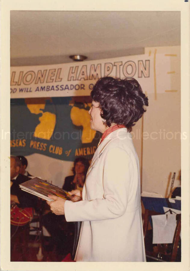 5 x 3 1/2 inch photograph. Lionel Hampton and band at the Overseas Press Club of America. A banner on the wall reads: Welcome Lionel Hampton, America's Good Will Ambassador of Jazz