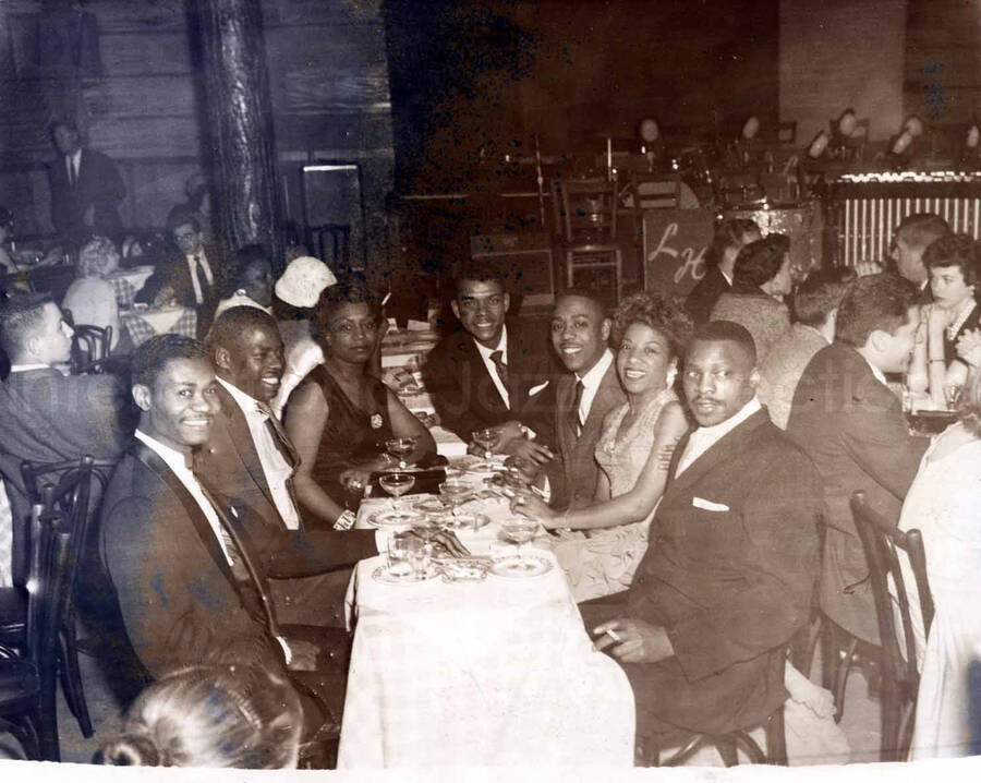 8 x 10 inch photograph. Leo Moore with unidentified persons in a restaurant. Accompanying this photograph is a portfolio from the Basin Street, 51st Street and Broadway