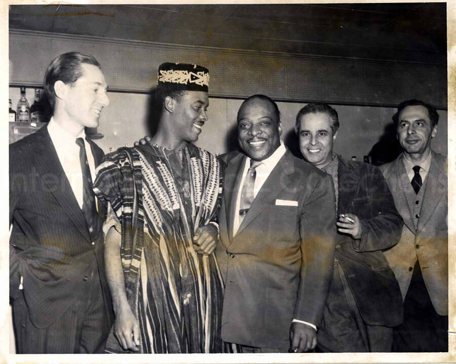 8 x 10 inch photograph. Leonard Feather (far left), Count Basie (center) with unidentified men, which includes one probably from West Africa. Accompanying this photograph is a portfolio from the Birdland. The portfolio is autographed by Steve Lawrence, Dick Hyman, Eddie Safranski, Al Klink, Count Basie, Don Lamond, Hymie Shertzer, and others