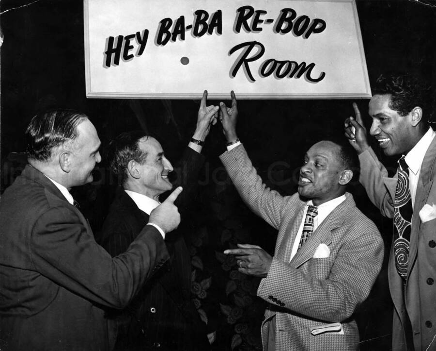 11 x 13 inch photograph. Lionel Hampton with Curley Hamner and two unidentified men. They are pointing to a sign that reads: Hey Ba-Ba Re-Bop Room