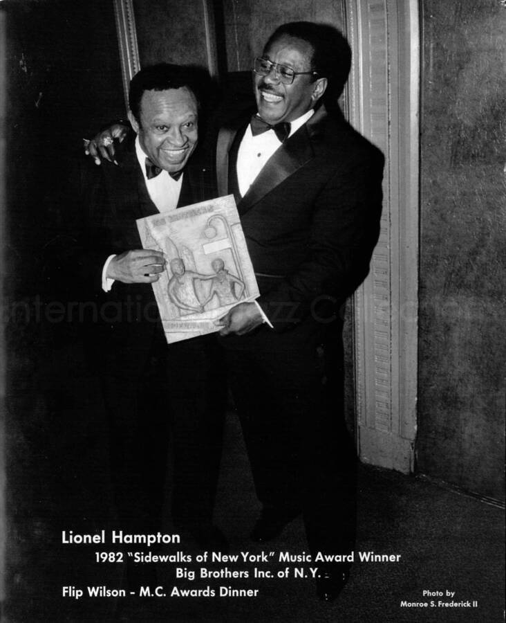 20 x 16 inch photograph. Lionel Hampton receiving the Big Brothers Sidewalks of New York Award from Flip Wilson on the occasion of the M. C. Awards Dinner. New York, NY. This photograph is mounted on cardboard