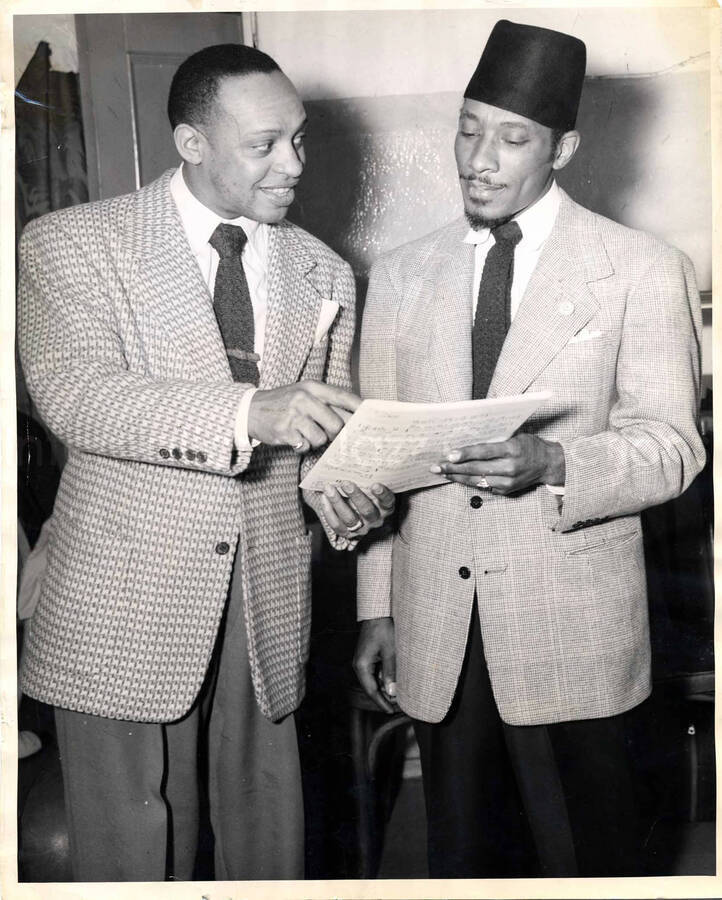14 x 11 1/4 inch photograph. Lionel Hampton with unidentified man [visiting a US Air Force base?]. The man is wearing a pin on his suit with the crescent moon with star symbol and a fez hat