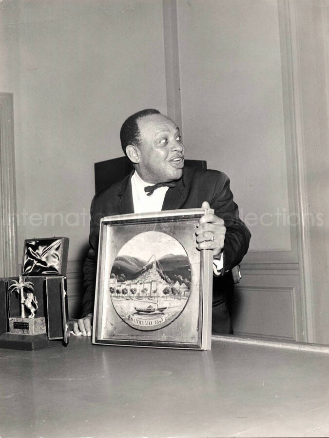 15 1/2 x 12 inch photograph. Lionel Hampton holding a framed picture [in San Remo, Italy?]. The picture reads: Sanremo 1845
