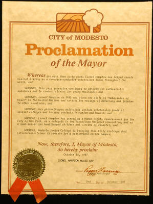 Certificate. 10 3/4"x8 1/4" Proclamation with gold foil Seal of the City of Modesto and orange ribbon in 16"x12" double mat City of Modesto proclaims October 28, 1987 as Lionel Hampton Music Day, on the occasion of his performance at Modesto Junior College. Peggy Mensinger, Mayor. Modesto, CA Oct. 2, 1987