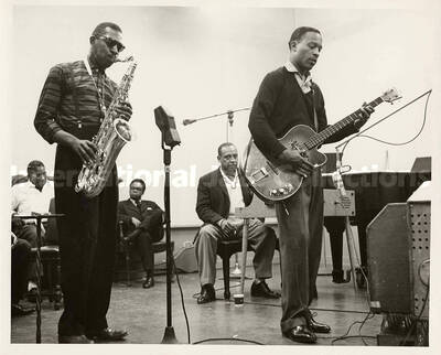 8 x 10 inch photograph. Lionel Hampton at the piano observing unidentified saxophonist and guitarist in a recording studio