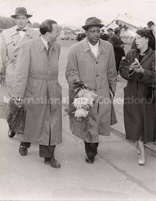 5 3/4 x 7 3/4 inch photograph. Lionel Hampton with unidentified persons, walking outside an airport [in Germany?]