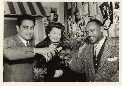 5 x 7 inch photograph. Lionel Hampton with unidentified persons [abroad?]. Hanging on a wall pictures of several artists