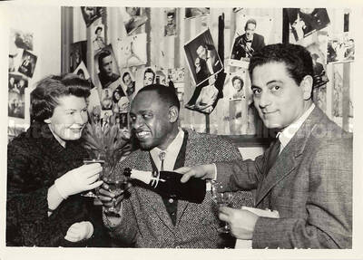 5 x 7 inch photograph. Lionel Hampton with unidentified persons [abroad?]. Hanging on a wall pictures of several artists