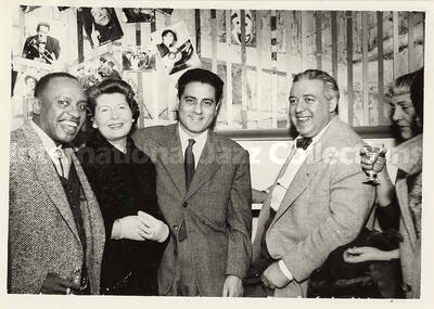 5 x 7 inch photograph. Lionel Hampton with unidentified persons [abroad?]. Hanging on a wall pictures of several artists