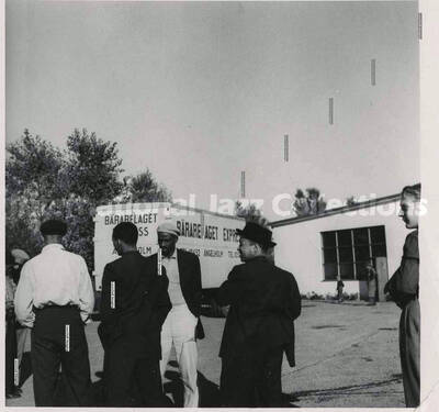 3 1/2 x 3 1/2 inch photograph. Lionel Hampton with unidentified men, [in Germany]. A Bararelaget Express truck is in the background