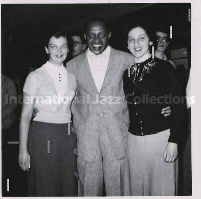 3 1/2 x 3 1/2 inch photograph. Lionel Hampton with two women, [in Canada]. Handwritten on the back of the photograph: Josi Bonomo (right), (Montreal); Joan Miller (left), (Montreal)